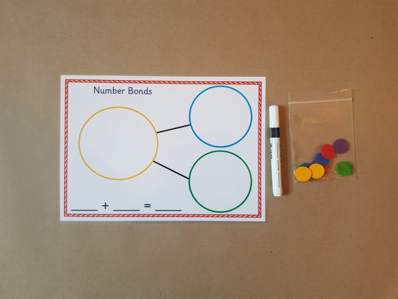 May include: Educational math game set featuring a worksheet with the text "Number Bonds" and colored circles. Includes a white marker and a bag of colorful circular counters. The worksheet has a red and white border.