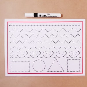 May include: A white dry-wipe marker lies above a white tracing practice sheet with a red border. The sheet has dotted lines for tracing patterns and shapes, including a rectangle, circle, and triangle.