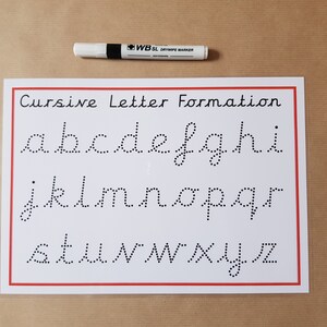 May include: A white drywipe marker lies above a white sheet with a red border. The sheet shows the cursive alphabet, from a to z, in dotted lines for tracing. The text "Cursive Letter Formation" is at the top.