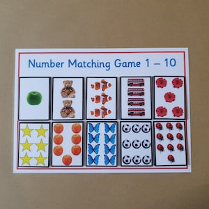 May include: A number matching game card with the title "Number Matching Game 1 - 10". The card features illustrations of various objects, including an apple, teddy bears, clownfish, buses, flowers, stars, oranges, butterflies, soccer balls, and ladybugs.