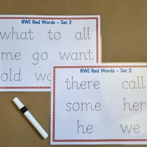 May include: Two white laminated educational sheets titled RWI Red Words - Set 2, featuring rows of dotted letters for tracing words like what, to, all, me, go, want, old, there, call, some, her, he, and we, accompanied by a white dry-erase marker.