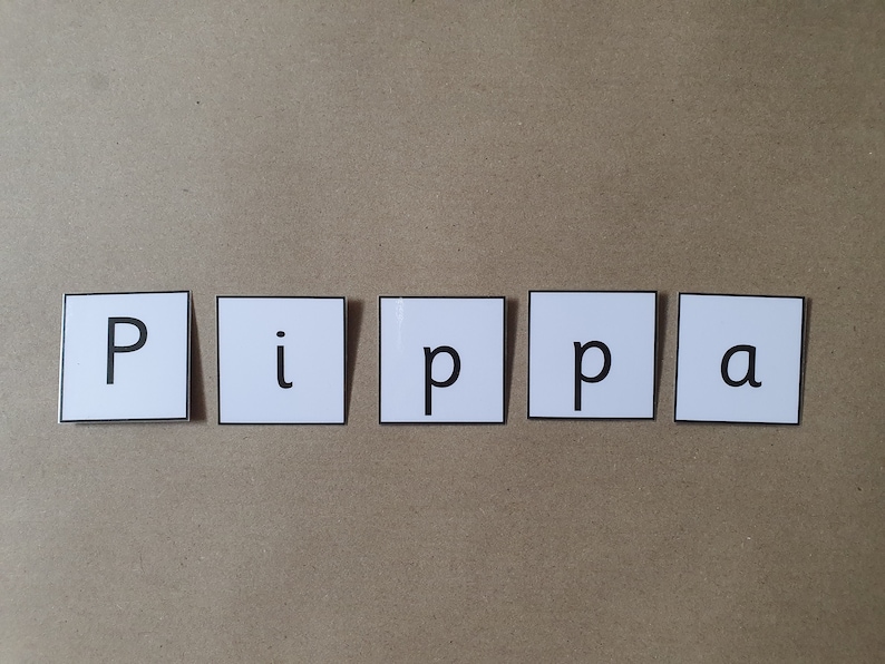 May include: Five white square tiles spelling the name "Pippa" in black capital letters and lowercase letters. The tiles are arranged horizontally on a light brown surface.