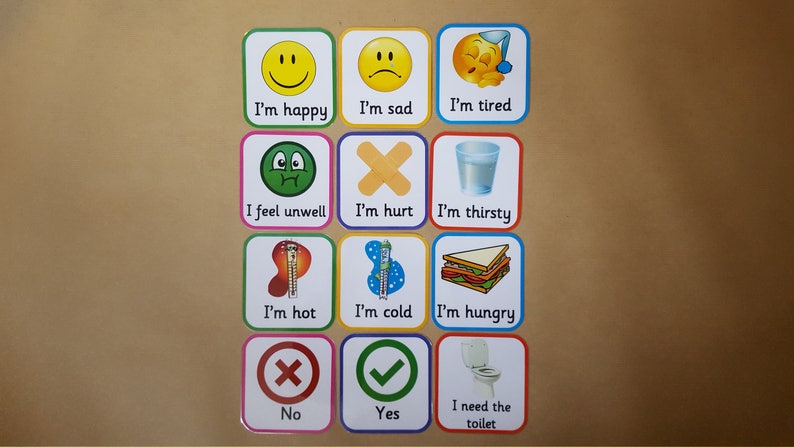 May include: A set of twelve square cards with various illustrations and text. The cards depict emotions and needs, including "I'm happy," "I'm sad," "I'm tired," "I feel unwell," "I'm hurt," "I'm thirsty," "I'm hot," "I'm cold," "I'm hungry," "No," "Yes," and "I need the toilet."