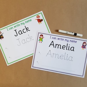 May include: Two white name tracing worksheets with the names "Jack" and "Amelia" printed in black. Each worksheet has a dotted line version of the name for tracing. Superhero graphics and the text "I can write my name" are also present.