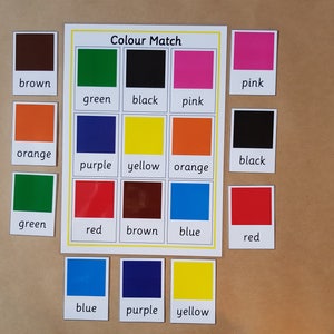 May include: A colour matching educational game with the text "Colour Match". The game includes cards with colour names like brown, green, black, pink, orange, purple, yellow, red, and blue. The cards are arranged on a brown surface.