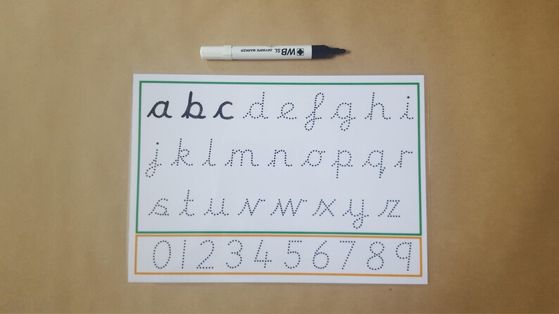 May include: A white sheet with the alphabet and numbers in dotted lines for tracing, with a green and orange border. A black and white marker is at the top. The letters are in lowercase, and the numbers are from 0 to 9.