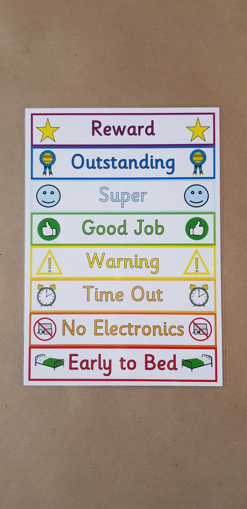 K&ouml;nnte beinhalten: Eine farbenfrohe Belohnungstafel mit Text wie "Belohnung", "Herausragend", "Super", "Gut gemacht", "Warnung", "Auszeit", "Keine Elektronik" und "Fr&uuml;h ins Bett". Die Tafel hat verschiedene Symbole.
