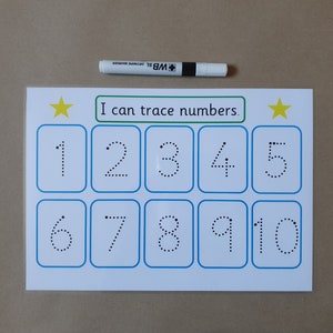 May include: A white educational tracing worksheet with the text "I can trace numbers." Features numbers 1-10 in dotted lines for tracing. A white and black marker is placed above the worksheet. Yellow stars are on the top corners.