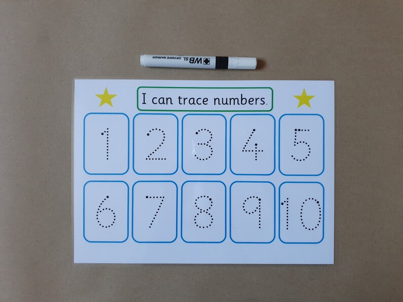May include: A white educational tracing worksheet with the text "I can trace numbers." Features numbers 1-10 in dotted lines for tracing. A white and black marker is placed above the worksheet. Yellow stars are on the top corners.