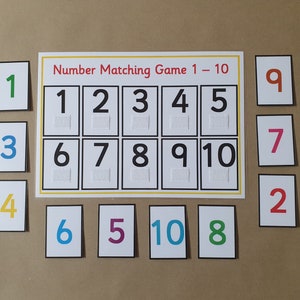May include: A number matching game labelled "Number Matching Game 1 - 10". The game features a central board with numbers 1-10 and matching cards. Each number is a different colour, with braille below.