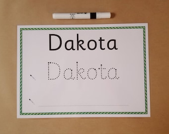May include: A white sheet of paper with the name "Dakota" printed in large, black letters and dotted letters below for tracing. A white marker with a black cap rests above the paper. The paper has a green border.