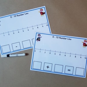 May include: Two white number line cards with blue borders, featuring a superhero graphic and the text "0-10 Number Line." One card shows a subtraction symbol, the other an addition symbol. A black marker is placed between the cards.