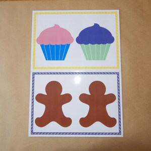 May include: Two cards with illustrations of baked goods. The top card features two cupcakes, one pink and one blue, with blue and green liners. The bottom card shows two brown gingerbread men with white borders and blue trim.