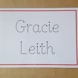 May include: A white card with a red border features the name "Gracie Leith" written in dotted letters. The card is set against a light brown background, presenting a clean and straightforward design.