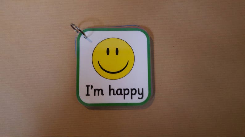 May include: A small, square card with rounded corners and a green border. The card features a yellow smiley face and the text "I'm happy" in black. A metal ring is attached to the top corner.