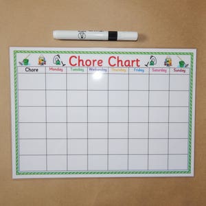 May include: A white chore chart with a green and white border, featuring the title "Chore Chart" in red. The days of the week are listed across the top. A white marker with a black cap rests above the chart.