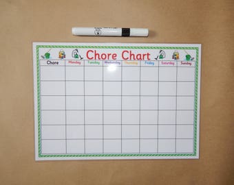 May include: A white chore chart with a green and white border, featuring the title "Chore Chart" in red. The days of the week are listed across the top. A white marker with a black cap rests above the chart.