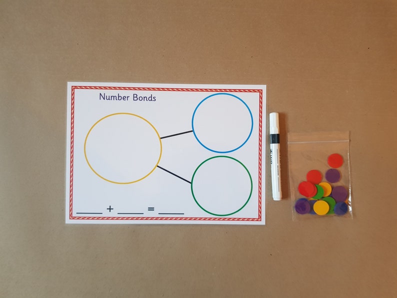 May include: Educational math set featuring a white card with "Number Bonds" text, circles, and an equation. Includes a white marker and a bag of colorful counters. Ideal for learning addition.