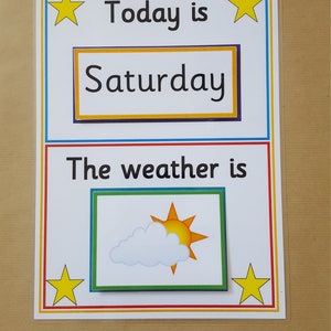 May include: A laminated educational chart with the text "Today is Saturday" and "The weather is." The weather section shows a sun and cloud graphic. Yellow stars and colorful borders frame the text.