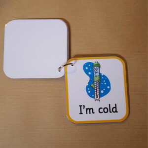 May include: A small, square flashcard with rounded corners and a yellow border. The card features a cartoon thermometer wearing a hat and scarf, with the text "I'm cold". A blank card is attached with a metal ring.