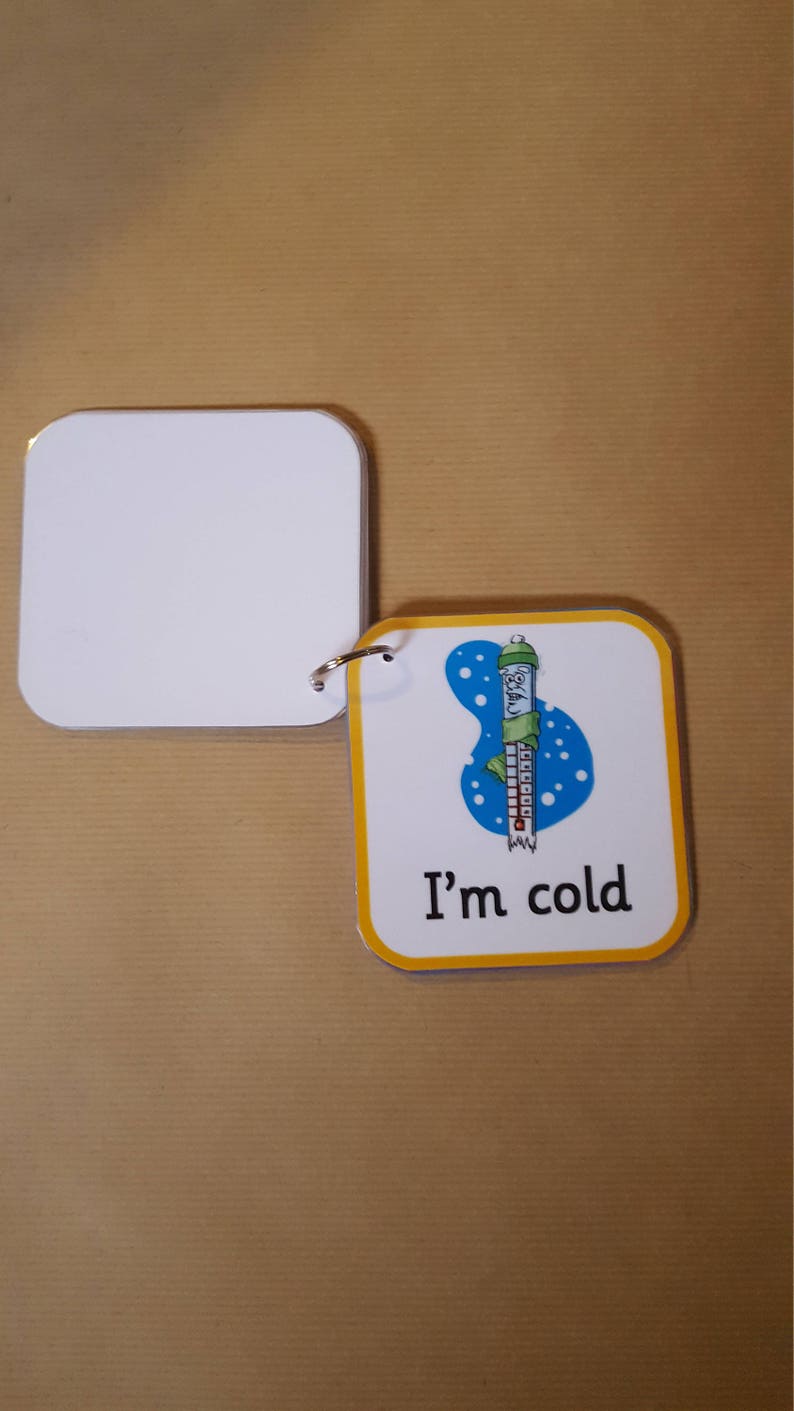May include: A small, square flashcard with rounded corners and a yellow border. The card features a cartoon thermometer wearing a hat and scarf, with the text "I'm cold". A blank card is attached with a metal ring.