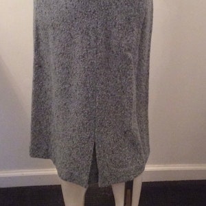 May include: A gray tweed skirt with a back slit. The skirt is on a mannequin and is displayed on a white platform.