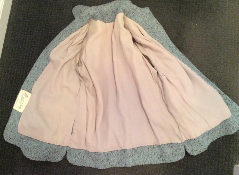 May include: A teal blue knitted jacket with a light pink lining. The jacket has a label that reads "Made in China".