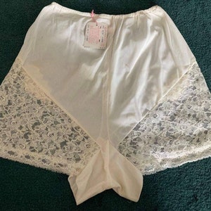 May include: White lace-trimmed underwear with a satin-like finish. The underwear has a wide waistband and a scalloped edge.