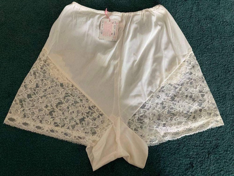 May include: White lace-trimmed underwear with a satin-like finish. The underwear has a wide waistband and a scalloped edge.