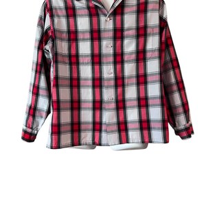 May include: A long-sleeved, button-down shirt in a red, black, and white plaid pattern. The shirt has a classic collar and buttoned cuffs. The garment is displayed on a white mannequin, showcasing the full front of the shirt.