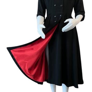 May include: Black vintage dress with a high collar and button details. The dress has three-quarter sleeves and a flared skirt. The inside lining is a vibrant red, creating a striking contrast. A classic and elegant garment.
