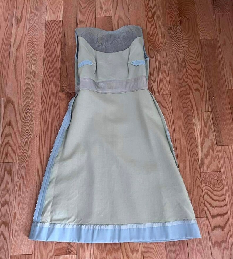 May include: A light blue sleeveless dress with a white lace bodice and a light green skirt. The dress has a zipper on each side and a white ribbon around the waist.