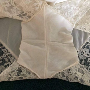 May include: White lace lingerie with a sheer, white fabric panel in the center. The lace is delicate and intricate, with a floral pattern.