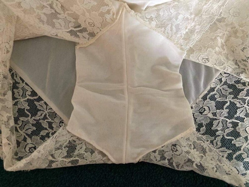May include: White lace lingerie with a sheer, white fabric panel in the center. The lace is delicate and intricate, with a floral pattern.