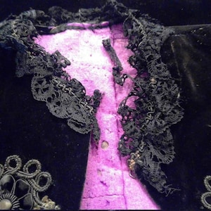 May include: Black velvet jacket with a lace trim and a pink lining. The jacket has decorative embellishments on the front.