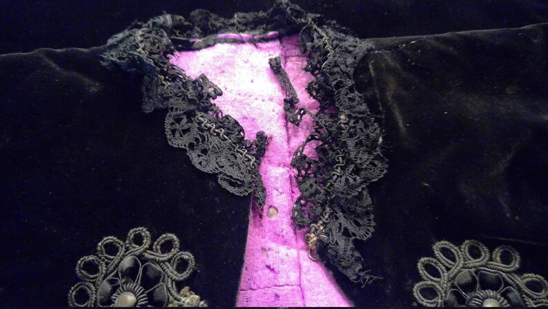 May include: Black velvet jacket with a lace trim and a pink lining. The jacket has decorative embellishments on the front.