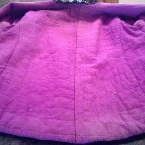 May include: The inside of a purple jacket with a black lining. The jacket is quilted and has a seam down the back.