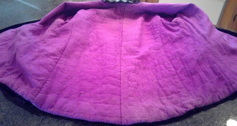 May include: The inside of a purple jacket with a black lining. The jacket is quilted and has a seam down the back.