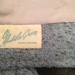 May include: A white label with the text "Natalie Green EXCLUSIVE" in black lettering on a light blue textured fabric.