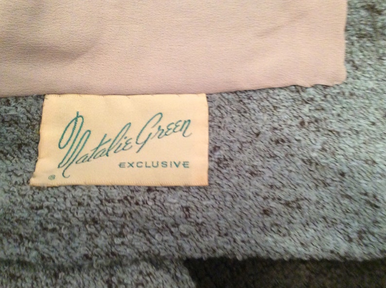 May include: A white label with the text "Natalie Green EXCLUSIVE" in black lettering on a light blue textured fabric.