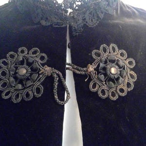 May include: Black velvet jacket with a lace collar and two black floral embellishments with black bead centers.