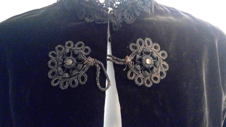 May include: Black velvet jacket with a lace collar and two black floral embellishments with black bead centers.