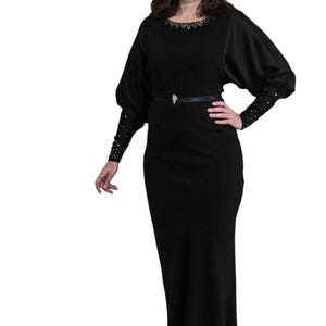 May include: A black long-sleeved dress with a jeweled neckline and a black belt. The dress has a fitted bodice and a flowing skirt.