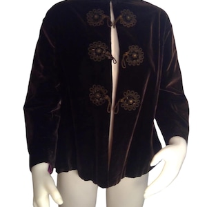 May include: A brown velvet jacket with a mandarin collar and decorative floral embellishments. The jacket has a front closure with a series of knotted cords.