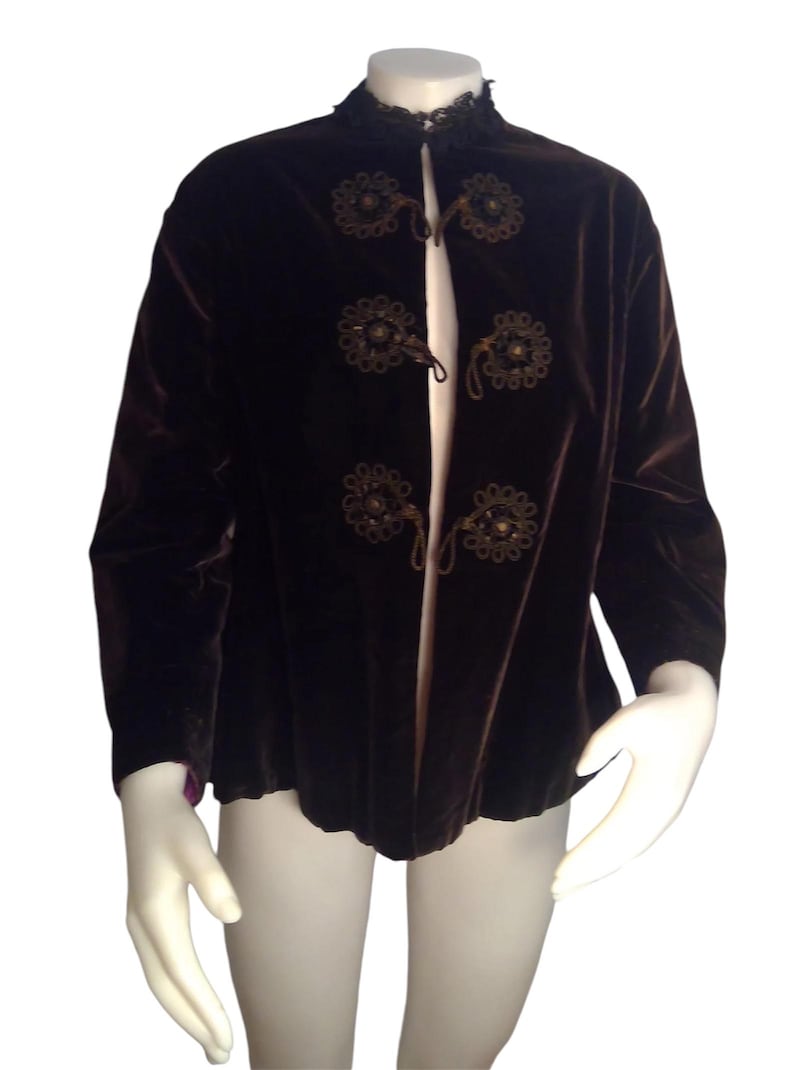 May include: A brown velvet jacket with a mandarin collar and decorative floral embellishments. The jacket has a front closure with a series of knotted cords.
