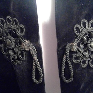 May include: A black velvet jacket with intricate black floral embroidery and tassel details on the front.