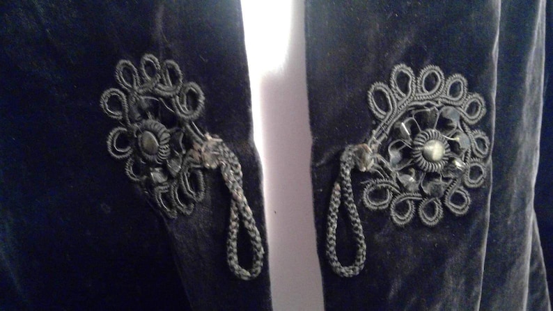 May include: A black velvet jacket with intricate black floral embroidery and tassel details on the front.