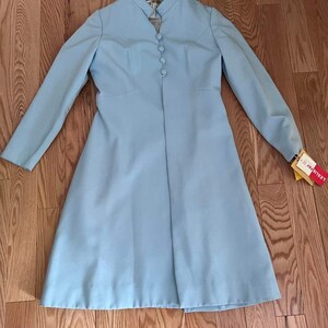 May include: A light blue long-sleeved coat with a mandarin collar and button closure. The coat has a fitted bodice and a flared skirt. The coat is laying flat on a wooden floor.