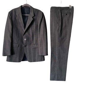 May include: A charcoal gray suit consisting of a single-breasted blazer with notched lapels, two front buttons, and two flap pockets, paired with matching straight-leg trousers featuring a waistband, a button closure, and side pockets.