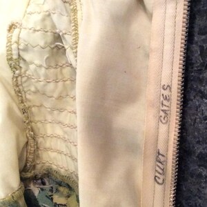 May include: Close-up of the inside of a garment with a floral print. The zipper is visible and has the text "COUTT GATES" printed on it.